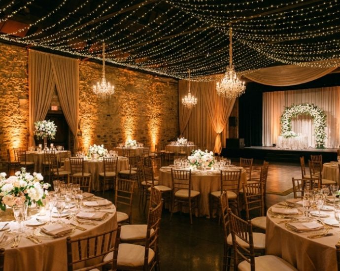 Elegant wedding reception hall illuminated by warm amber uplighting and twinkling ceiling fairy lights.